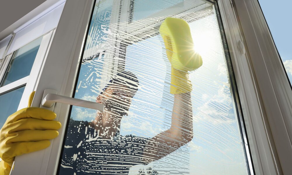 Ein Fenster wird von einer Person in gelben Handschuhen mit einem Schwamm bei strahlendem Wetter gereinigt. | © Adobe Stock/ New Africa