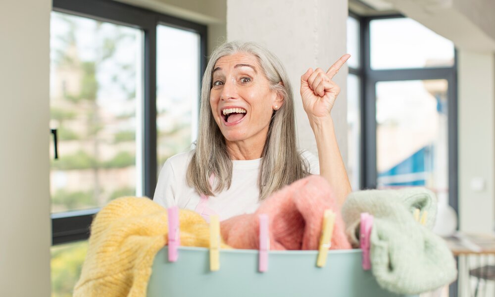 Ältere Frau mit Wäschekorb voller bunter Wäsche | © Adobe Stock/ kues1