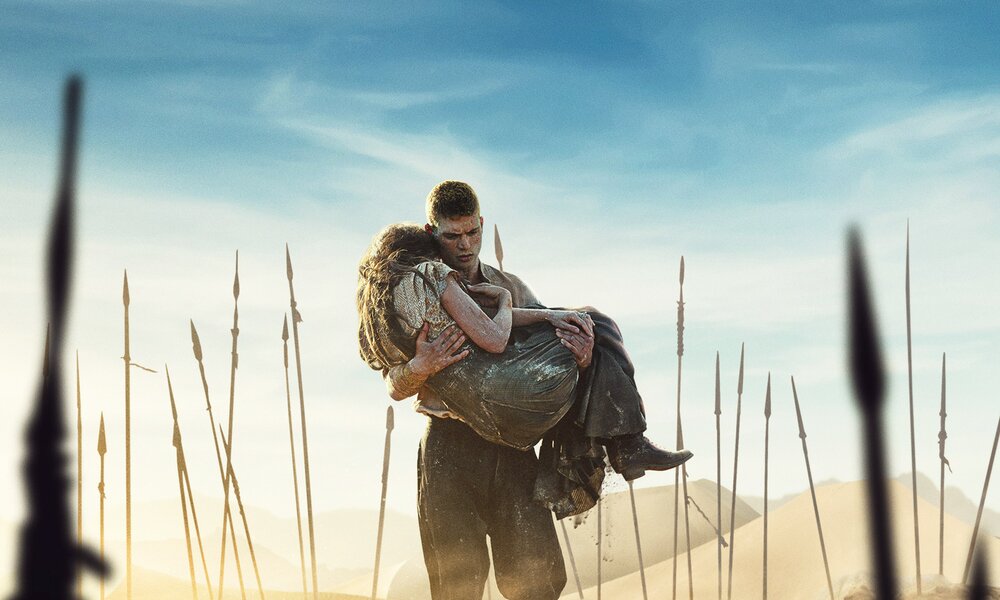 Josha Stradowski trägt Madeleine Madden  durch den Wüstensand umgeben von Speeren auf der Key Art zur 3. Staffel Prime Video Serie "Das Rad der Zeit" | © Amazon Prime Video