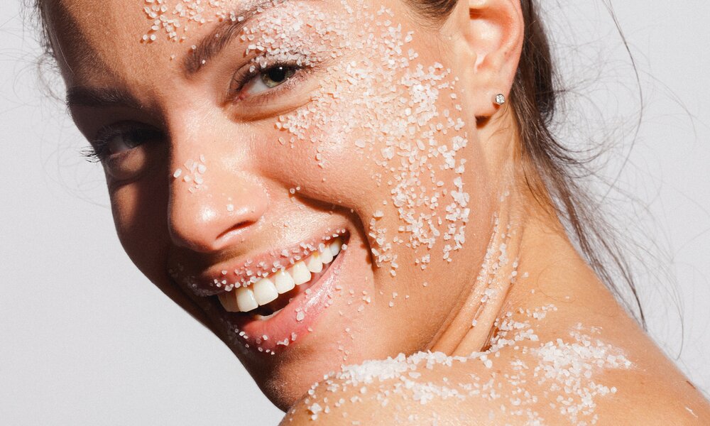 Schöne und junge Frau lächelt in die Kamera. Sie hat grobes Salz im Gesicht und trägt einen kleinen Ohrring. Der Hintergrund ist grau hinterlegt und sie hat braune Haare und helle Augen. | © Getty Images / gruizza