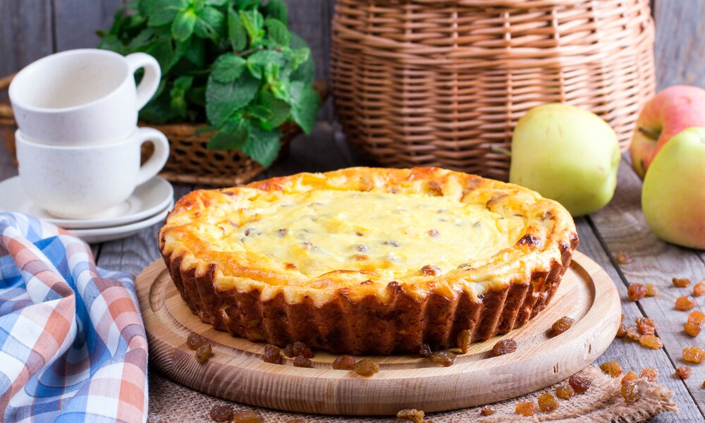 Auf einem Tisch angerichtet, befindet sich eine cremige Tarte. Daneben finde sich Tassen, ein Korb und Äpfel. | © Getty Images / Qwart
