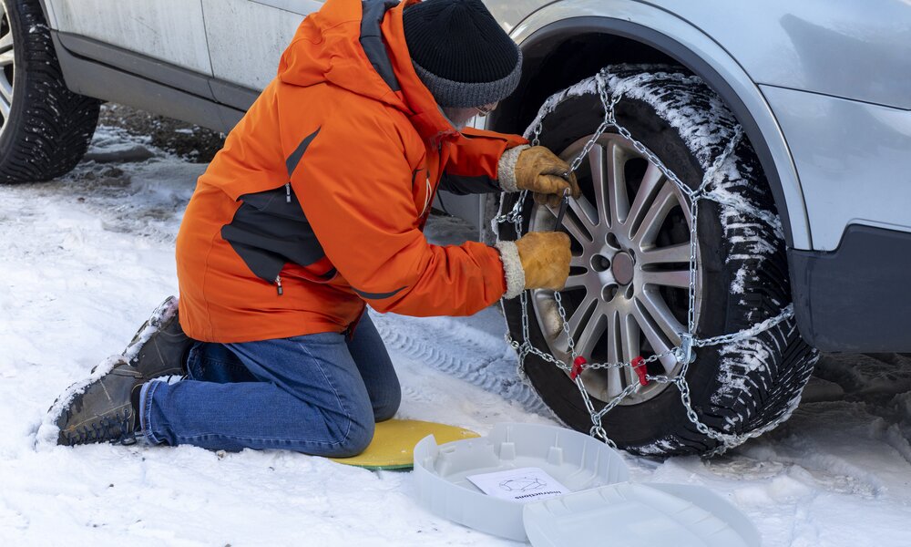 Mann bringt Schneeketten an Auto an  | ©  Getty Images / SolStock