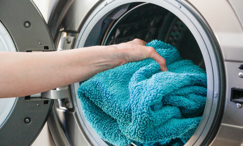 Frau legt Handtuch in Waschmaschine | ©  Getty Images/ 	Kinga Krzeminska