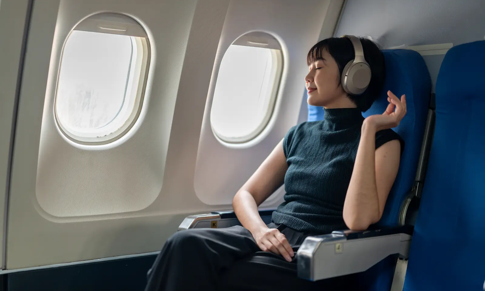 Frau entspannt mit Flugzeug-Gadets während eines Fluges | © adobe.stock.com/Wasana