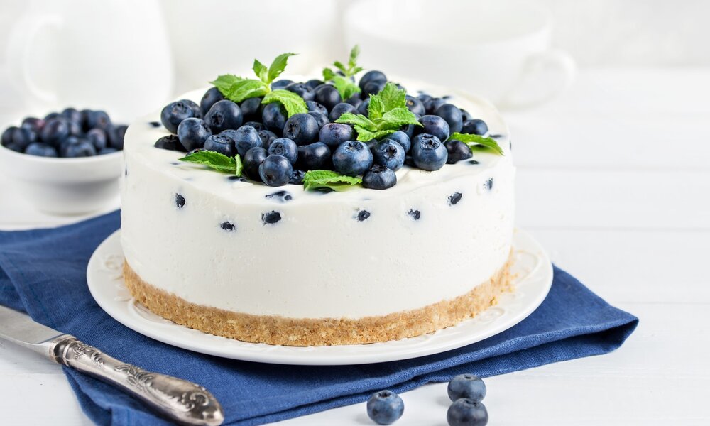 Low Carb Glück: Cremiger Quarkkuchen ohne Zucker und ohne Mehl | © Getty Images / 	Anna_Shepulova Angeschnittener Quarkkuchen belegt mit vielen frischen Blaubeeren. | © Getty Images / 	Anna_Shepulova
