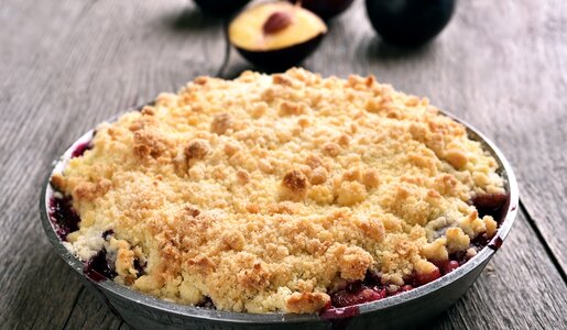 Pflaumencrumble in einer Blechauflaufform, dahinter frische Pflaumen. | © Getty Images / voltan1