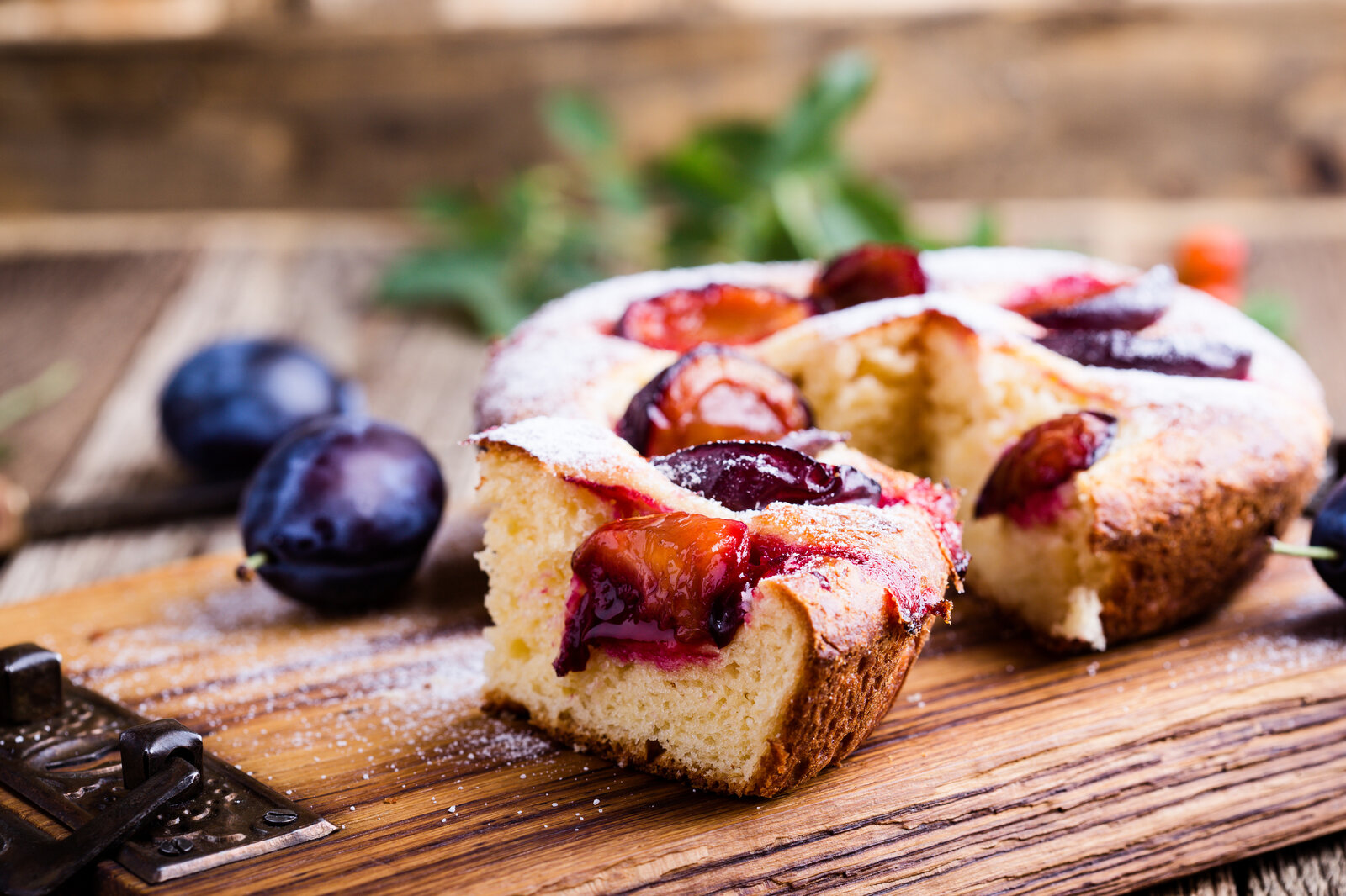 Kleiner angeschnittener luftiger Pflaumenkuchen daneben frische Pflaumen. | © Getty Images / istetiana