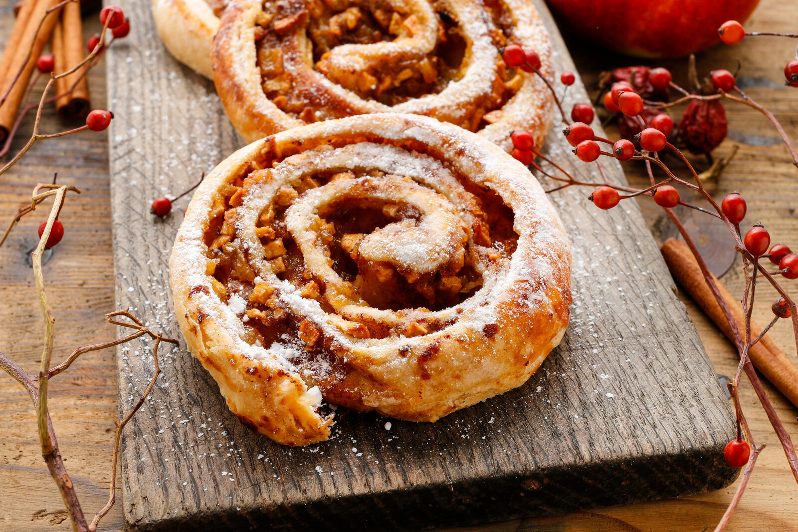 Drei Apfelschnecken auf einem rustikalem Holzbrett angerichtet und mit Puderzucker bestäubt, in herbstlicher Atmosphäre. | © Adobe Stock / agneskantaruk