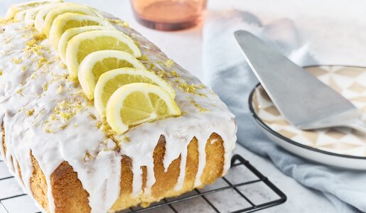 Auf einem Kuchengitter angerichteter Zitronen-Buttermilchkuchen mit Zitronenguss überzogen und mit Zitronenraspeln garniert. | © Getty Images / Tim Young Photography