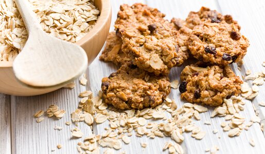 Mehrere Haferflocken-Kekse nebeneinander, daneben eine Holzschale mit Haferflocken und einem Holzlöffel. | © Adobe Stock / Jiri Hera