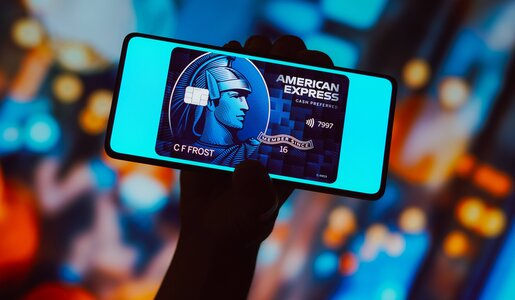 Hand hält Smartphone mit digitaler American Express Blue Card vor verschwommenem, buntem Hintergrund. | © IMAGO/Zoonar
