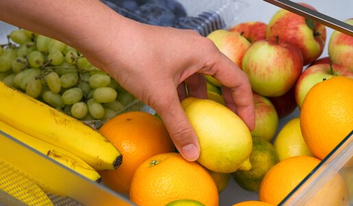 Eine Hand greift in eine Schublade voller bunter Früchte, darunter Zitronen, Bananen, Trauben und Äpfel. | © Adobe Stock/ rosinka79
