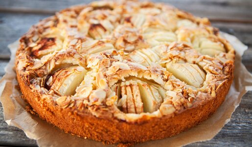 Ein versunkener Apfelkuchen mit einem Topping aus Mandelblättchen auf einem mit Backpapier ausgelegten Unterteil einer Backform. | © Adobe Stock / PapadoXX