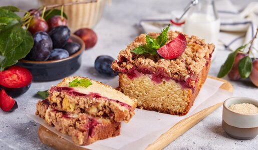Angeschnittener Kuchen mit Pflaumen in herbstlicher Ambiente, dahinter frische Pflaumen und Milch. | © Adobe Stock / natkinzu