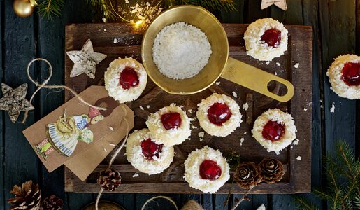 Mehrere mit roter Füllung bespritzte Kekse in weihnachtlicher Umgebung, daneben Schale mit Kokosraspeln. | © 	Isabell Triemer