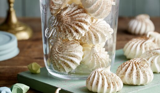 Baiser-Hauben mit Zimt bestäubt in einem Weck-Glas, einige weitere daneben auf einem Teller. | © Isabell Triemer