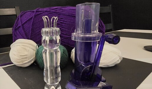 Eine durchsichtige Strickliesel und eine blaue Strickmühle stehen auf einem weißen Tisch vor bunter Wolle | © Sabrina Forst