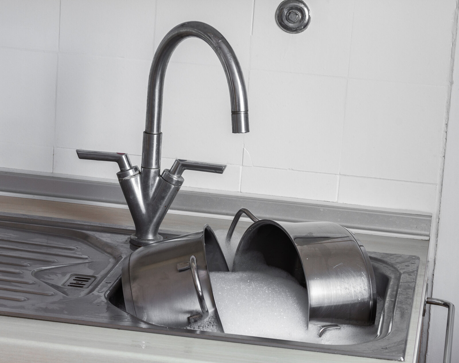 Eine silbernes Waschbecken in der Küche mit laufendem Wasser, in der Spüle liegen Töpfe in einem Schaumbad | © Adobe Stock/blende11.photo