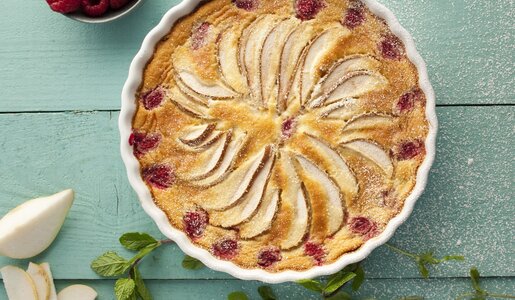 Birnen-Himbeer-Kuchen von oben in einer weißen Kuchenform auf einem Tisch angerichtet. | © Getty Images / 	Portugal2004