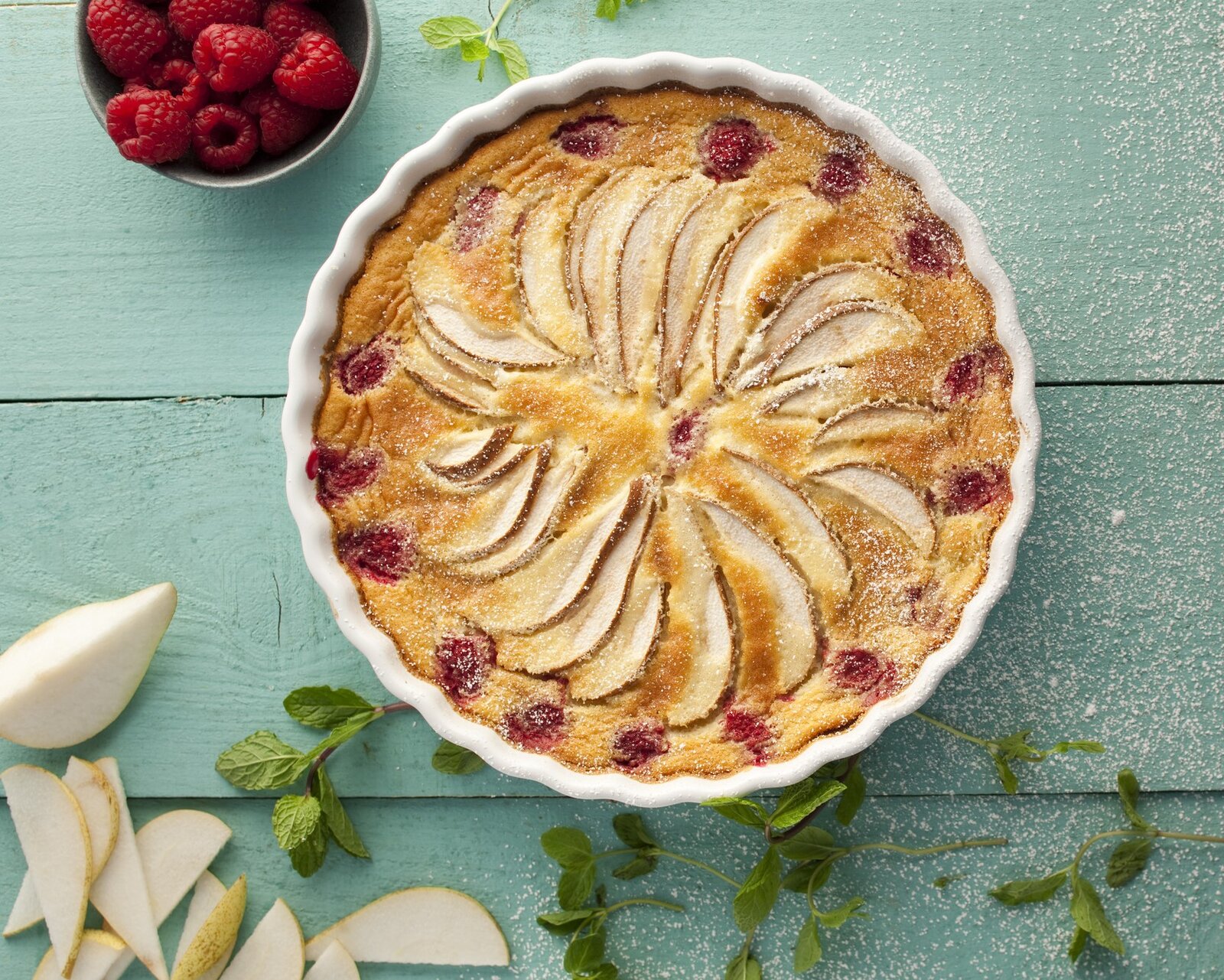 Birnen-Himbeer-Kuchen von oben in einer weißen Kuchenform auf einem Tisch angerichtet. | © Getty Images / 	Portugal2004