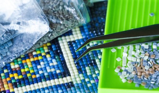 Nahaufnahme eines Mosaikprojekts mit bunten Steinchen, einer grünen Sortierschale, Pinzette und Plastiktüten im Hintergrund. | © ANGHI /stock.adobe.com