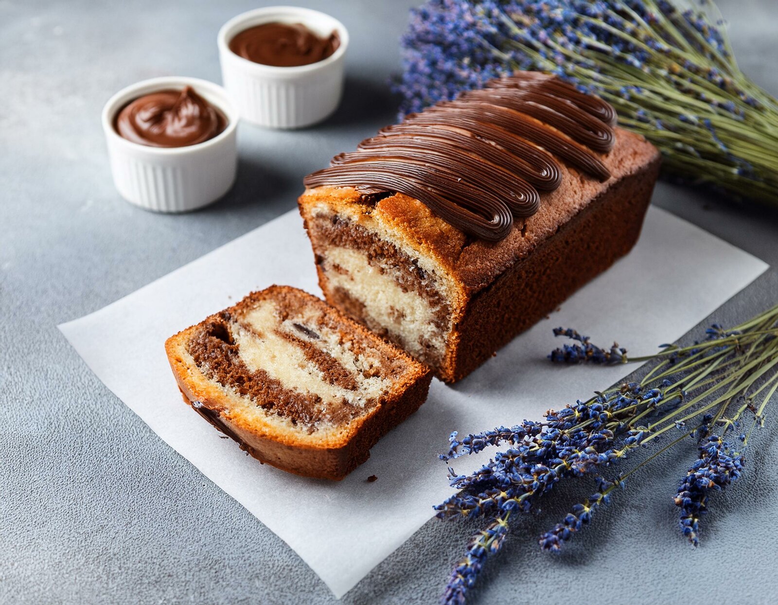 Angeschnittener Nutella-Kuchen in Kastenform auf einem Holzuntergrund, daneben Nutella und Lavendel. | © Adobe Stock / Jeri / KI generiert
