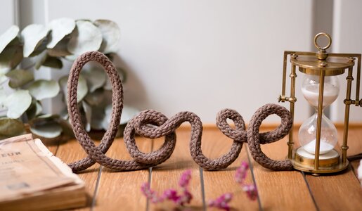 Schriftzug "love" aus braunem Seil auf Holzuntergrund, daneben eine goldene Sanduhr und Eukalyptusblätter im Hintergrund. | © Nastasia Froloff /stock.adobe.com 