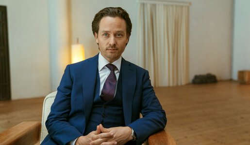 Tom Schilling als Björn Diemel sitzt ernst blickend auf einem Holzstuhl in einem minimalistischen Raum. | © Netflix / Achtsam Morden