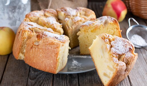 In Stücke geschnittener Apfel-Rührkuchen auf einem Teller angerichtet, mit Puderzucker bestreut. | © Getty Images / Qwart