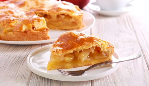 Stück Apfelkuchen vor einem ganzen Kuchen auf einem Tisch. | © Adobe Stock / manyakotic