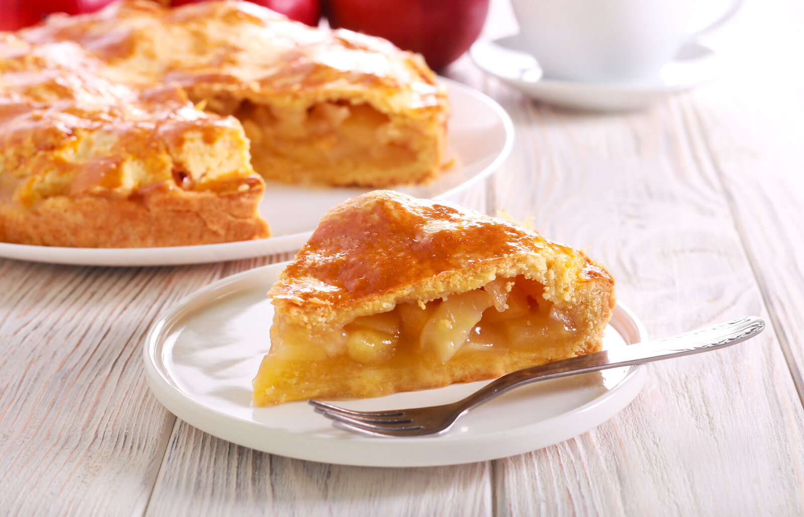Stück Apfelkuchen vor einem ganzen Kuchen auf einem Tisch. | © Adobe Stock / manyakotic
