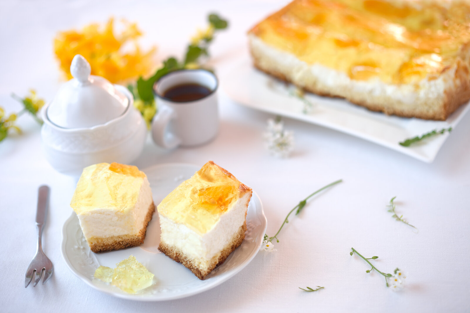 Zwei Stücke Mandarinen-Schmandkuchen auf einem Teller, dahinter der ganze Kuchen. | © Adobe Stock /  rainbow33