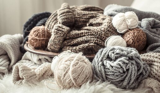 Verschiedene Wollknäuel und gestrickte Kleidungsstücke in sanften Naturfarben sind auf flauschigem Untergrund arrangiert. | © puhimec/stock.adobe.com