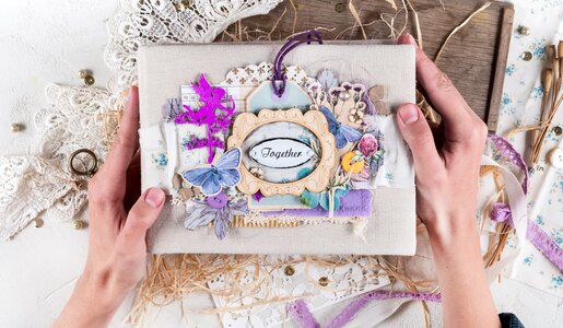 Zwei Hände halten ein kunstvoll verziertes Scrapbook mit floralen Details, Spitze und dem Schriftzug „Together“ in elegantem Rahmen. | © Svetlana Glazkova /stock.adobe.com