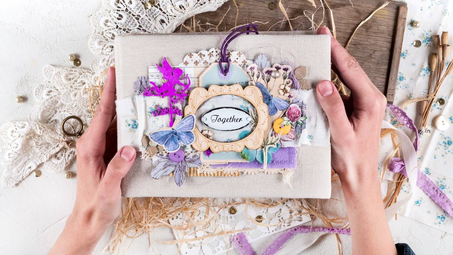 Zwei Hände halten ein kunstvoll verziertes Scrapbook mit floralen Details, Spitze und dem Schriftzug „Together“ in elegantem Rahmen. | © Svetlana Glazkova /stock.adobe.com