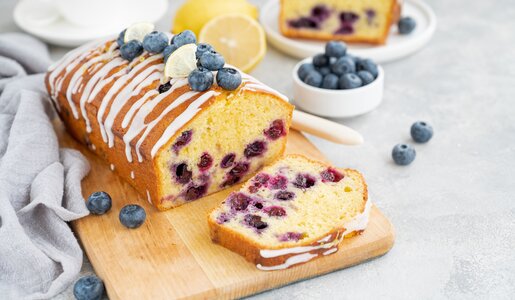 Angeschnittener Blaubeer-Kuchen auf einem Brett, daneben und dahinter frische Blaubeeren und Zitronen | © Getty Images / 	Irina Taskova