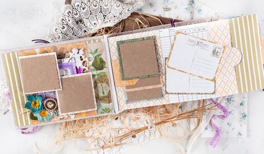 Ein kunstvoll gestaltetes Scrapbook mit Vintage-Elementen, Stoffblumen und Spitzenband liegt offen auf einer weißen Oberfläche mit Holzelementen. | © Svetlana Glazkova/stock.adobe.com