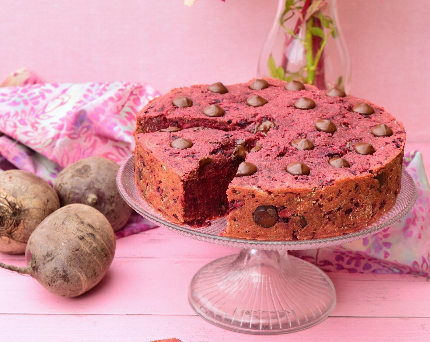 Rote-Bete-Kuchen steht auf einem Kuchenteller. Der Hinterggrund ist rosa und neben dem Kuchen liegt frische Rote-Bete. | © Getty Images / AmalliaEka