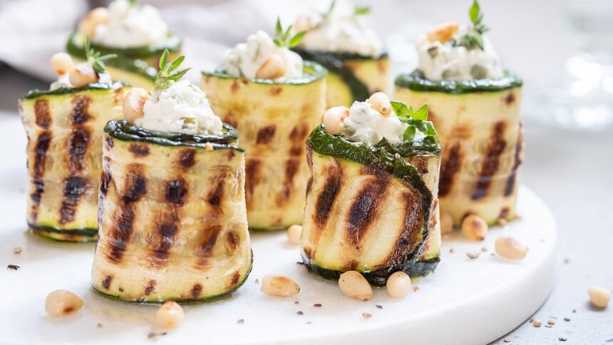 Gegrillte Zucchini-Röllchen befüllt mit Fetakäse, drapiert auf einem weißen Teller, in Nahaufnahme. | © Getty Images / Azurita