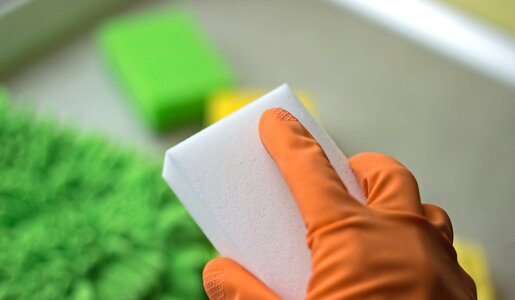 Hand mit orangenem Putzhandschuh hält einen Schmutzradierer | ©  Getty Images / Irina Vodneva