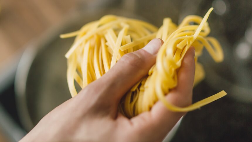 Eine Hand hält Pasta über einen Topf mit kochendem Wasser | © Getty Images/nerudol