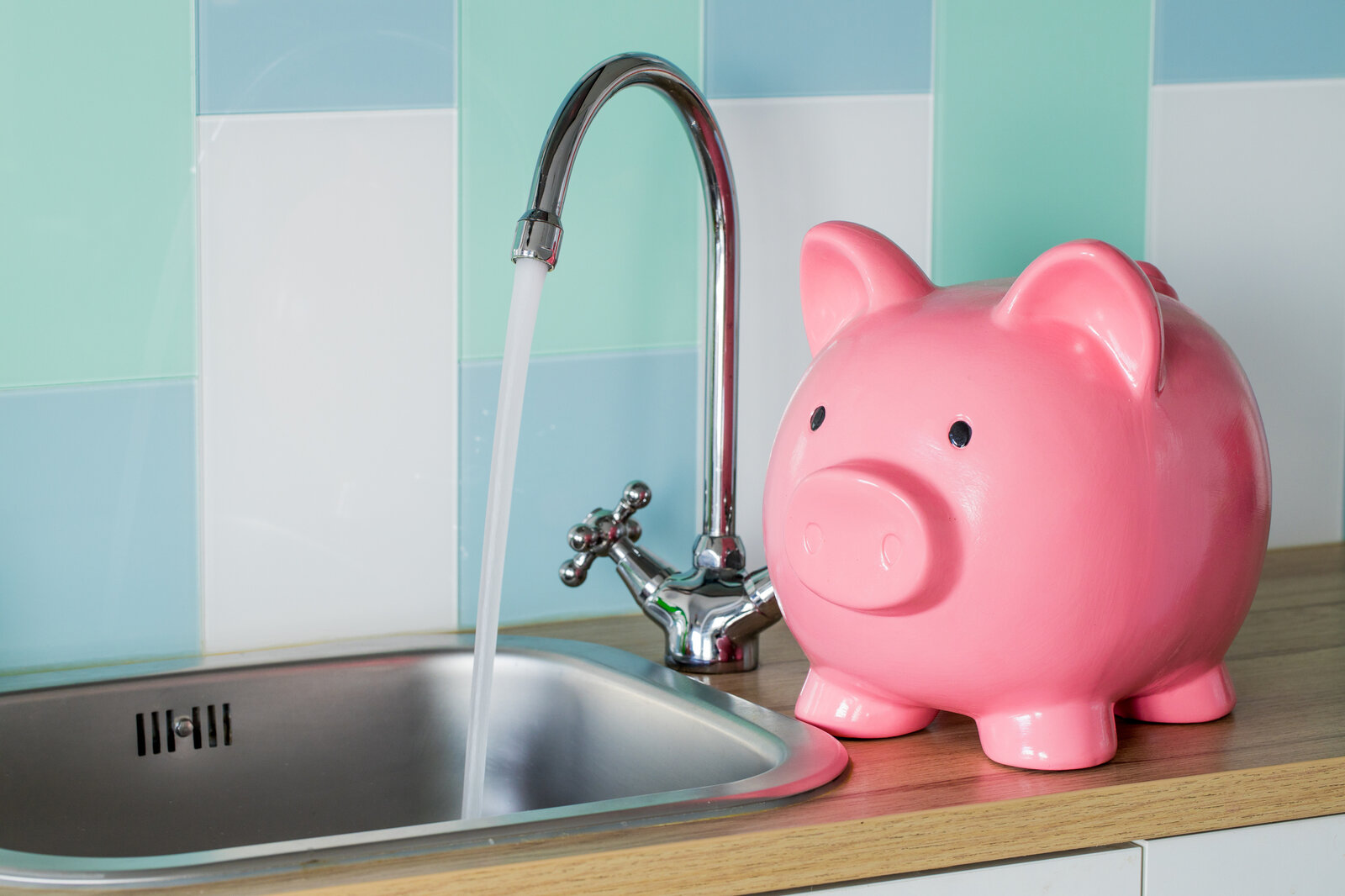 Sparschwein steht neben einem laufenden Wasserhahn  | ©  Getty Images / Andrzej Rostek
