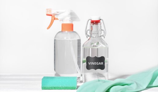 Essig und Sprühflasche stehen auf einem Tisch, davor Putzhandschuhe | ©  Getty Images / Yulia Panova
