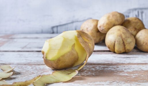 Eine halbgeschälte Kartoffel, im Hintergrund ein Haufen ungeschälter Kartoffeln | © Getty Images / Caterina Oltean / 500px