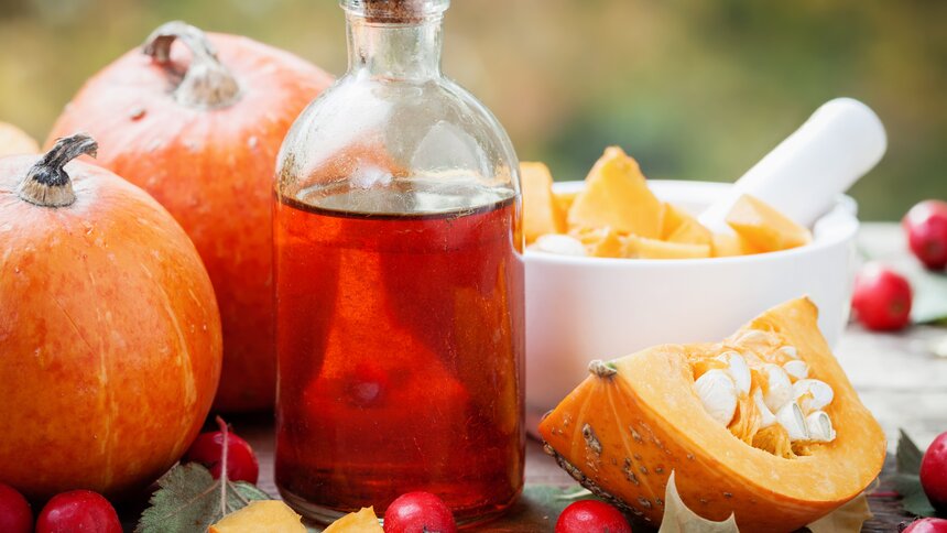 Eine Flasche befüllt mit Öl steht im Vordergrund vor aufgeschnittenen Kürbissen. | © Getty Images / ChamilleWhite