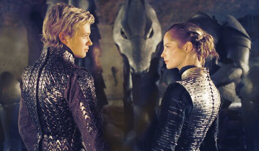 Edward Speleers und Sienna Guillory in silbernen Rüstungen stehen mit dem Rücken zum Betrachter in einem dunklen Raum und unterhalten sich in einer Szene aus dem Kinofilm "Eragon" | © ddp images/0th Century Fox/David Appleby