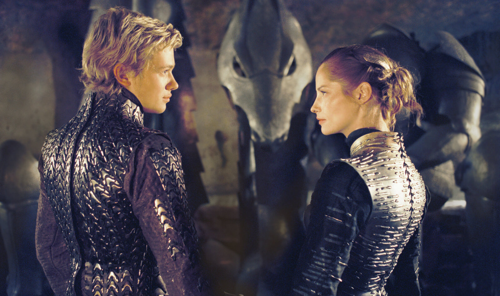 Edward Speleers und Sienna Guillory in silbernen Rüstungen stehen mit dem Rücken zum Betrachter in einem dunklen Raum und unterhalten sich in einer Szene aus dem Kinofilm "Eragon" | © ddp images/0th Century Fox/David Appleby