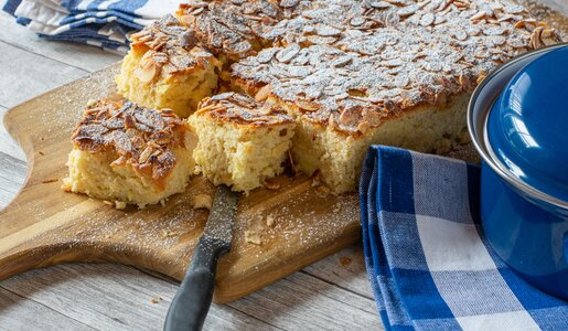 Angeschnittener Apfelkuchen mit Mandelsplittern liegt auf einem Holzbrett. | © Getty Images / Angelika Heine