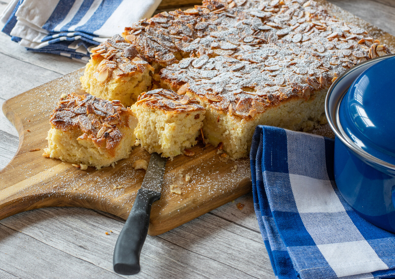 Angeschnittener Apfelkuchen mit Mandelsplittern liegt auf einem Holzbrett. | © Getty Images / Angelika Heine