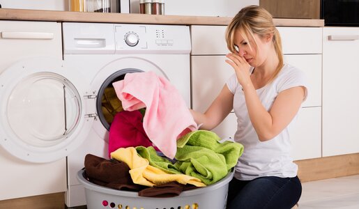 Frau holt Wäsche aus der Maschine und hält sich die Nase zu | ©  Getty Images / AndreyPopov